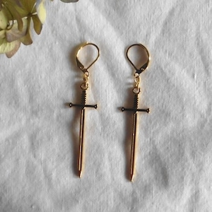 May include: A pair of gold sword earrings. The swords have a simple design with a cross guard and a pointed tip.