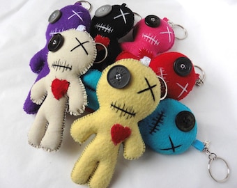 May include: A group of seven colorful felt voodoo dolls with button eyes and stitched mouths. Each doll has a red heart sewn on the front and a key chain attached.