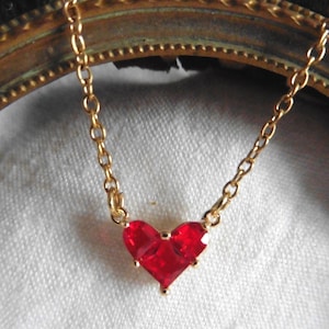 Peut inclure: Un collier en chaîne dorée avec un pendentif en forme de cœur rouge.