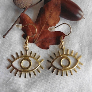 Puede incluir: Pendientes de oro en forma de ojo con un diseño detallado. Los pendientes cuelgan de una hoja y una bellota marrones.