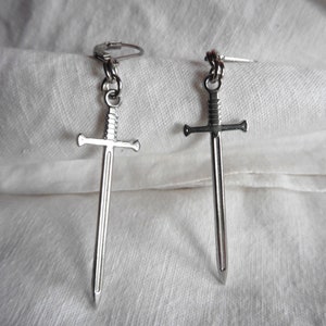 May include: A pair of silver sword earrings. The swords have a simple design with a pointed tip and a cross guard.
