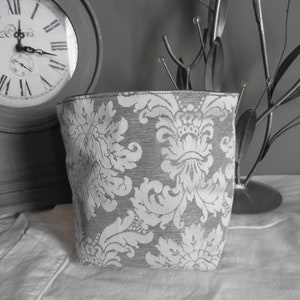 Peut inclure: Un panier de rangement en tissu gris avec un motif damassé blanc. Le panier est posé sur une surface blanche.