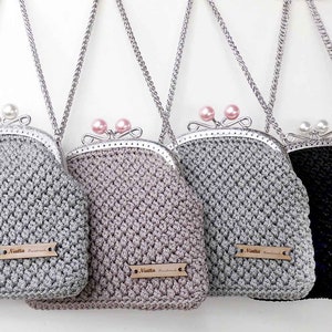 May include: Four crocheted purses with silver chains and clasps. The purses are in silver, light brown, gray, and black. Each purse has a small wooden tag with the text "Autto Handmade" on it.