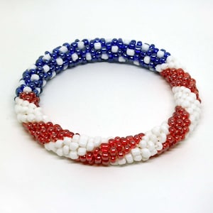 May include: A red, white and blue beaded bracelet with a spiral design. The bracelet is made of small, round beads.
