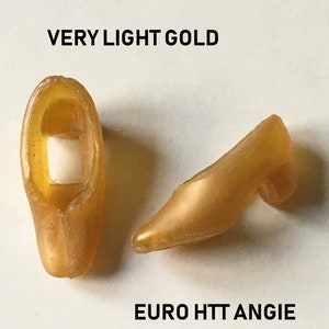 May include: A pair of gold-colored high-heeled shoes. The shoes are made of a smooth, shiny material. The shoes are labeled "VERY LIGHT GOLD" and "EURO HTT ANGIE".