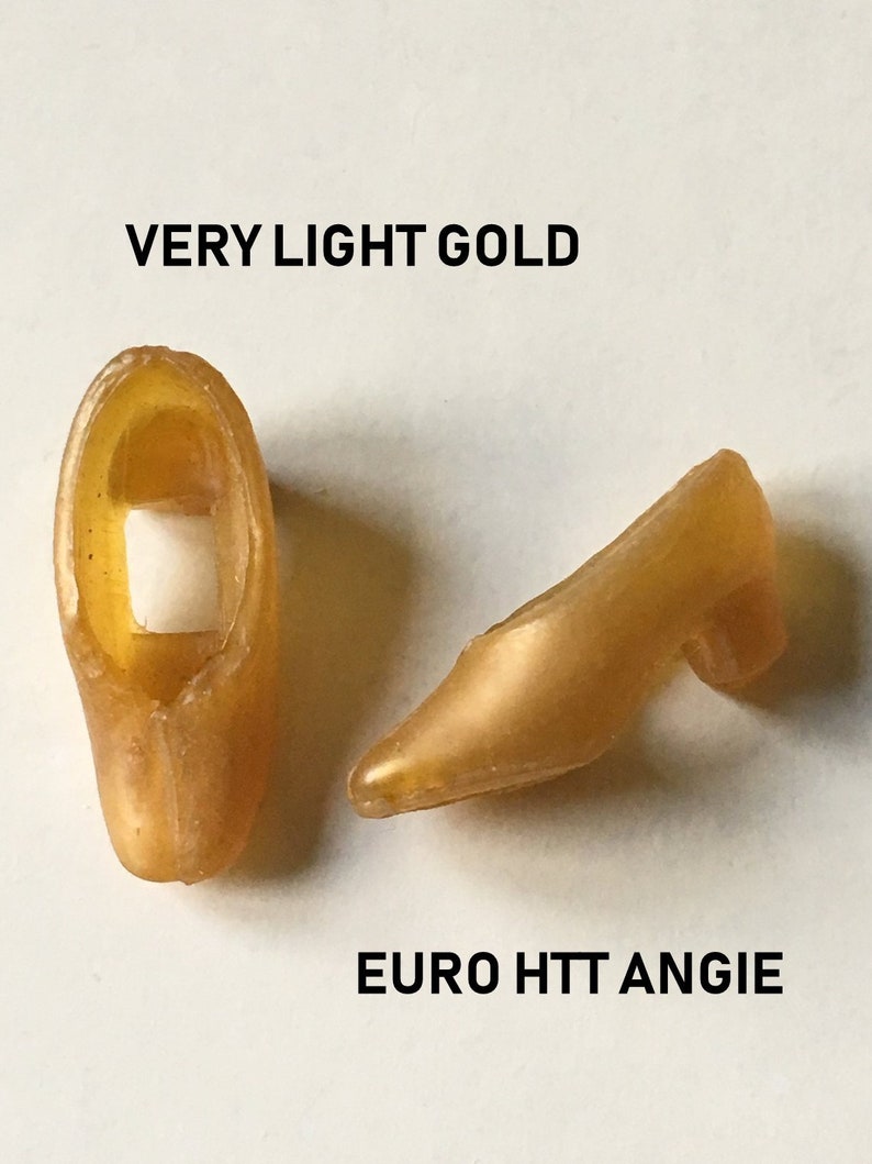 May include: A pair of gold-colored high-heeled shoes. The shoes are made of a smooth, shiny material. The shoes are labeled "VERY LIGHT GOLD" and "EURO HTT ANGIE".