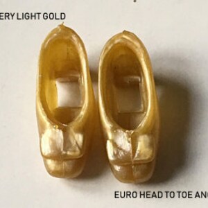 May include: Pair of gold-colored plastic doll shoes with a bow detail. The shoes are labeled "VERY LIGHT GOLD" and "EURO HEAD TO TOE ANGIE".