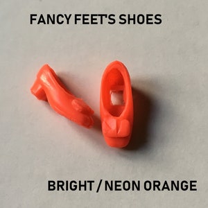 May include: A pair of bright orange plastic doll shoes. "FANCY FEET'S SHOES" and "BRIGHT/NEON ORANGE" are printed on the white background.