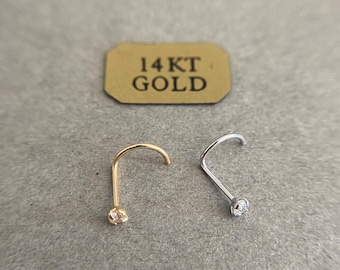 May include: Two nose rings with small clear stones. The nose ring on the left is gold and the nose ring on the right is silver. The label reads "14KT GOLD".