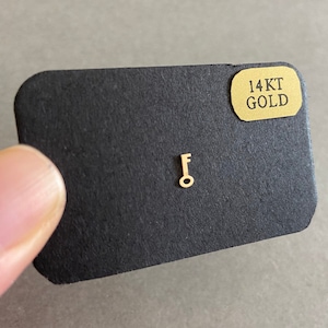 May include: A small gold key charm on a black card with the text "14KT GOLD" on a gold label.