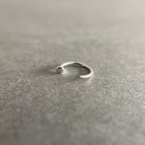 May include: A silver nose ring with a small, round bead at the end.
