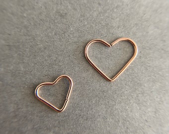 Pode incluir: Dois aros de coração de ouro, um maior que o outro, sobre um fundo cinza.