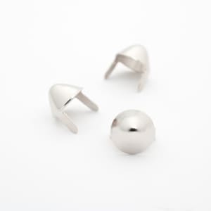 Puede incluir: Tres remaches de metal plateado, dos con puntas puntiagudas y uno con punta redondeada.