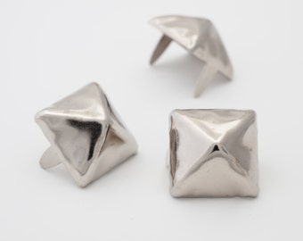 May include: Three silver pyramid-shaped metal studs with a pointed top and a flat base. The studs have a shiny finish and are designed for attaching to fabric or leather.