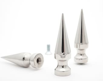 May include: Three silver metal spikes with a pointed tip and a rounded base. The spikes are on a white surface.