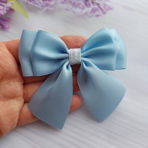 Peut inclure: Un nœud en satin bleu clair avec un centre en paillettes argentées. Le nœud est noué avec une seule boucle et est parfait pour ajouter une touche d'élégance à toute occasion.