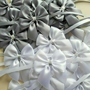May include: A collection of white and gray satin ribbon bows with silver glitter accents. The bows are tied with long ribbons, perfect for adding a touch of elegance to gifts or crafts.