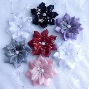 Puede incluir: Un surtido de accesorios para el cabello con flores de tela hechas a mano en varios colores. Las flores presentan pétalos en capas, adornos centrales brillantes y están en tonos de blanco, negro, rojo, rosa, gris y morado. Estas flores decorativas son ideales para ocasiones especiales.