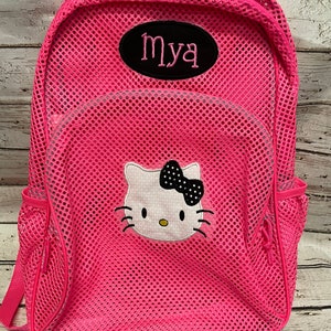 May include: A bright pink mesh backpack featuring a Hello Kitty design with a black bow and the name "Mya" embroidered on a black oval patch. The backpack has side pockets and a zippered main compartment.