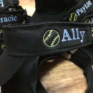 May include: Black visor hats embroidered with names and a softball design. The name "Ally" is embroidered in light blue, with a yellow softball graphic. Other names like "Lilly", "Gracie", "Payton", "Jaycee", "Hudson", and "Taylor" are also visible.
