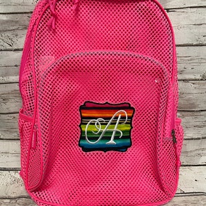 May include: Bright pink mesh backpack with a zippered main compartment, side pockets, and a front patch. The patch features a rainbow striped design with a white script letter "A".