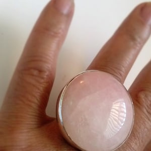 May include: A large, round, pink gemstone ring with a silver setting. The ring is worn on a finger.
