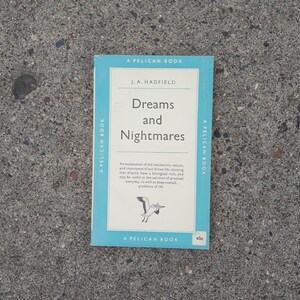 May include: A blue and white book titled "Dreams and Nightmares" by J.A. Hadfield. The book is part of the Pelican Book series.