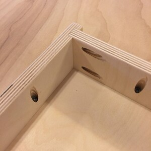 K&ouml;nnte beinhalten: Nahaufnahme einer Eckverbindung in einer Holzkiste, die die Taschenl&ouml;cher und Schrauben zeigt, die zum Zusammenbauen der Kiste verwendet werden.