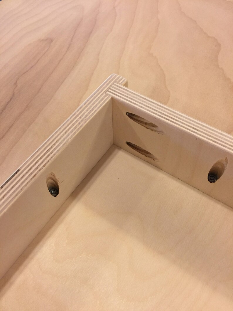 K&ouml;nnte beinhalten: Nahaufnahme einer Eckverbindung in einer Holzkiste, die die Taschenl&ouml;cher und Schrauben zeigt, die zum Zusammenbauen der Kiste verwendet werden.