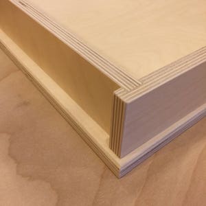 K&ouml;nnte beinhalten: Eine Holzkiste mit einer Schublade, die herausgezogen werden kann. Die Kiste ist aus hellem Holz gefertigt und hat eine glatte Oberfl&auml;che.