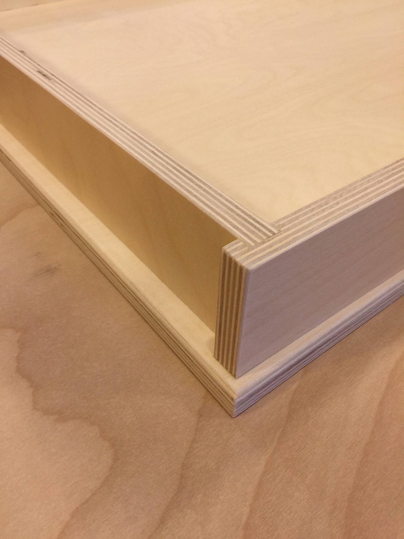 K&ouml;nnte beinhalten: Eine Holzkiste mit einer Schublade, die herausgezogen werden kann. Die Kiste ist aus hellem Holz gefertigt und hat eine glatte Oberfl&auml;che.