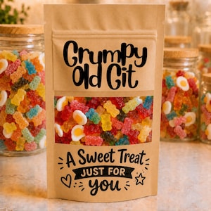 Op de afbeelding: Een bruine papieren stazak gevuld met kleurrijke gummisnoepjes, waaronder beertjes en gebakken eivormen. De voorzijde bevat zwarte tekst met "Grumpy Old Git" en "A Sweet Treat JUST FOR you" met decoratieve hart- en sterpictogrammen.