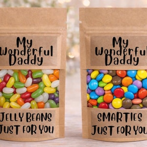 Puede incluir: Dos bolsas de papel marrón llenas de caramelos de colores. Una bolsa contiene gominolas, la otra Smarties. Cada bolsa tiene una etiqueta que dice "My Wonderful Daddy" y "Just For You". El fondo está borroso con luces bokeh.
