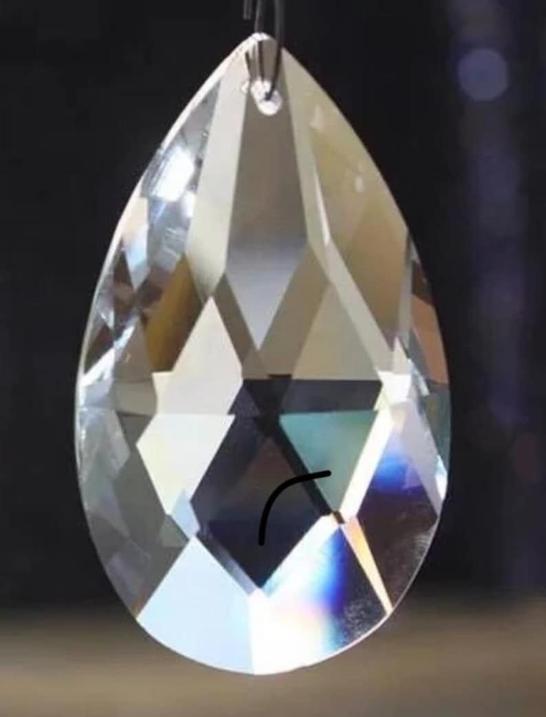 May include: A clear crystal teardrop prism with a faceted design. The prism has a silver metal loop at the top for hanging.