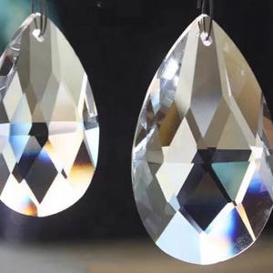Puede incluir: Dos colgantes de cristal transparente facetado con forma de l&aacute;grima. Cada colgante presenta un peque&ntilde;o orificio en la parte superior para colgarlo y muestra superficies geom&eacute;tricas multifacetadas que refractan la luz con bordes definidos.