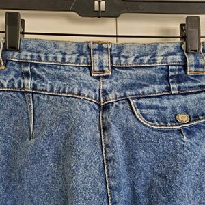 May include: A pair of blue denim jeans with a back pocket and a button closure. The jeans have a faded look and a light wash.