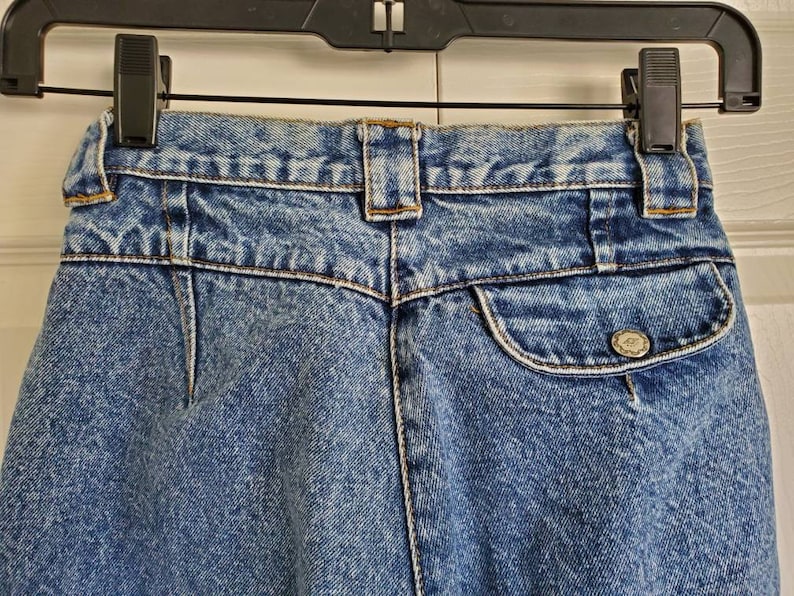 May include: A pair of blue denim jeans with a back pocket and a button closure. The jeans have a faded look and a light wash.