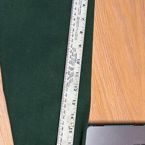 May include: Dark green sweater sleeve with patches. A ruler shows the sleeve is approximately 24 inches long. Patches include text that reads "USA" and "SCOUT".