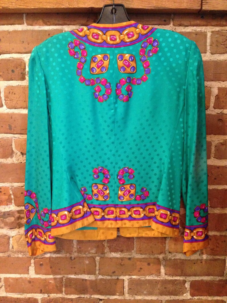 May include: A teal blue silk blouse with a gold chain and jewel pattern. The blouse has a polka dot pattern and a mandarin collar.