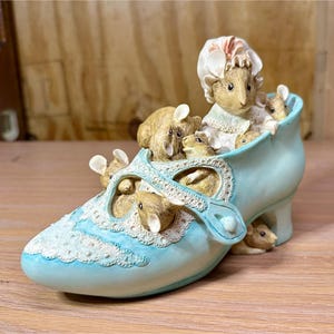 May include: A light blue ceramic shoe figurine filled with several small mice. The shoe has a decorative lace design on the front and a small heel. The mice are various shades of brown and tan, with some wearing bonnets.