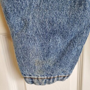 May include: Close-up of the bottom of a pair of light blue denim jeans. The denim has a faded, distressed look. The jeans have a brown seam around the hem.