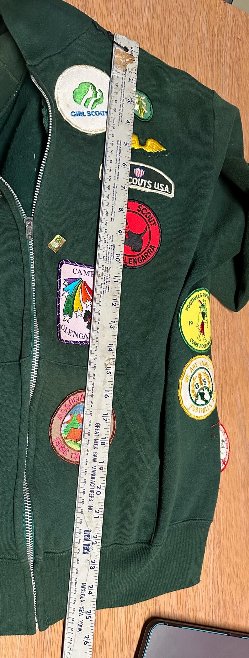 May include: Dark green zip-up jacket with multiple patches, including "Girl Scout" and "Scouts USA." Patches feature colorful designs and text. The jacket is approximately 25 inches long.