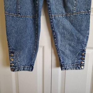 May include: A pair of light blue denim pants with a distressed look. The pants have a button detail on the bottom of each leg.