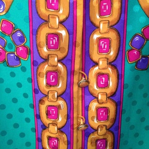 May include: A close-up of a fabric with a repeating pattern of gold chains, pink and purple squares, and teal polka dots.