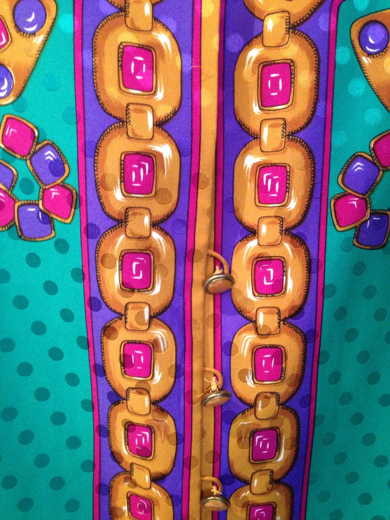 May include: A close-up of a fabric with a repeating pattern of gold chains, pink and purple squares, and teal polka dots.
