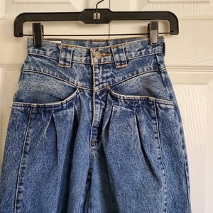 May include: A pair of blue denim jeans with pleats and multiple pockets. The jeans have a high waist and a relaxed fit.