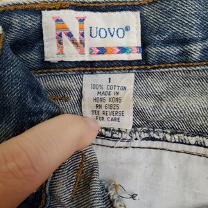 May include: A close-up of a blue denim jean waistband with a white tag that reads "UOVO&reg;" and "100% COTTON MADE IN HONG KONG RN 61825 SEE REVERSE FOR CARE".