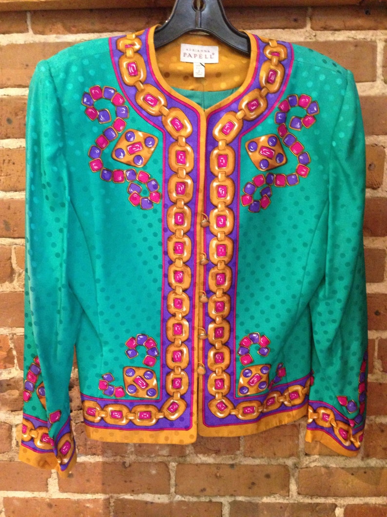 May include: A teal green blazer with a polka dot pattern and a gold, purple, and pink chain design. The blazer has a button closure and long sleeves. The label reads "Adrienne Vittadini PAPELL".