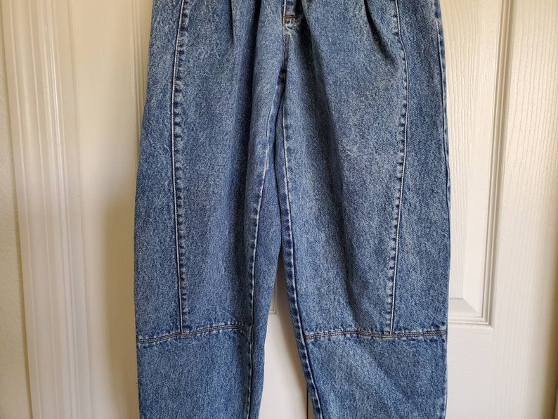 May include: A pair of light blue denim jeans with a distressed look. The jeans have a high waist and a relaxed fit. They feature a pleated front and a straight leg.