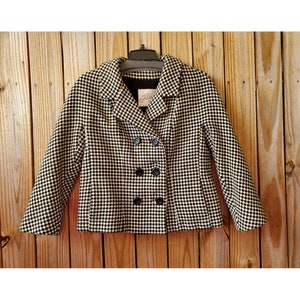 May include: A black and white checkered double-breasted jacket with a black collar and buttons. The jacket is hanging on a hanger against a wood background. The label "Shelly" is visible on the inside of the jacket.